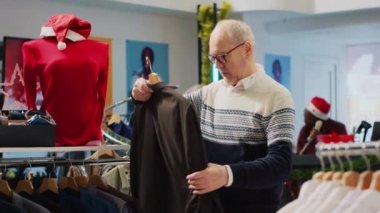 Kış Noel tatilinde kıyafet mağazasında tişört karıştıran, moda mevsimlik kıyafetlere bakan, perakende terapi yapan, alışveriş tavsiyesi arayan kıdemli bir adam.
