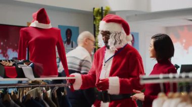 Noel Baba gibi giyinmiş Afrikalı bir çalışan, Noel 'de Noel alışverişinde müşterilere kıyafet seçmesinde yardımcı oluyor. Moda dükkanında müşteriye yardım eden işçi