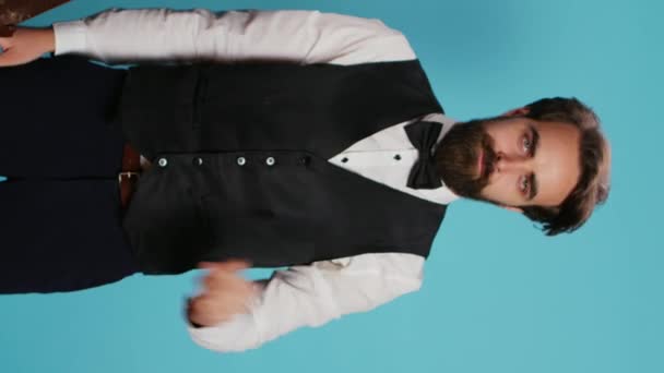 垂直ビデオBellboyは 青い背景に対する停止サインを示すために手を挙げ 広告に取り組み カメラで解雇ジェスチャーを表現します 従業員のドアマンは拒否を示しています トロリー — ストック動画