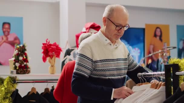 上了年纪的夫妇在圣诞装潢服装店购物时 为儿子找到了完美的圣诞礼物 他们高兴极了 客户在寒假期间浏览衣服 — 图库视频影像