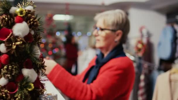 上了年纪的女人在寒假期间买时髦的领带送给圣诞礼物的丈夫 圣诞装潢服装店的资深顾客在寻找礼物 — 图库视频影像