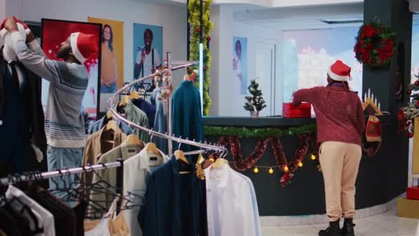アフリカ系アメリカ人の同僚は ショッピングモールの衣料品店でクリスマスの装飾を準備しています お祝いの精神気分の従業員 またはXmasの装飾とファッションブティックを締めくくる — ストック動画