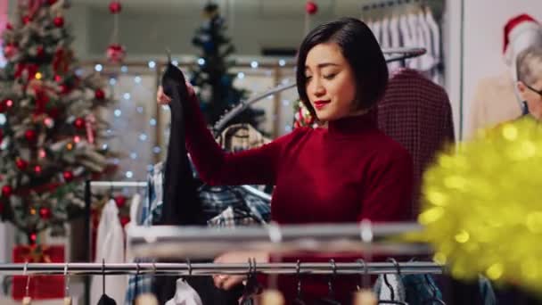 Asian Client Browsing Rack Clothes Christmas Themed Shop Checking Fitting — Stock Video