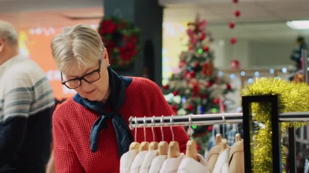 冬のホリデーシーズンの間 Xmasの衣料品店で服をブラウジングする高齢女性 ショッピングのシニアクライアント モールのクリスマス装飾ファッションブティックでスリーセッション — ストック動画
