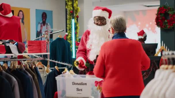 小売アシスタントは サンタクロースとしてドレスを着て 寄付箱でクライアントから不要な服を集め クリスマスシーズン中に必要なものにプレゼントし ホリデーチアを広める — ストック動画