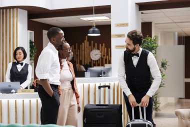 Otelde valiz taşıyan otel görevlisi lobideki resepsiyondaki konuklara bavullarını taşımalarına yardım etmeyi teklif ediyor. Bellboy turistlere ve yük arabalarına lüks hizmet veriyor..