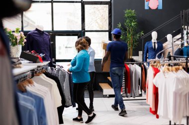 Afro-Amerikan kurye müşteri siparişlerini tutuyor, alışveriş merkezinden ayrılıyor. Teslimat üniforması giyen bir adam, modern butikte müşteri paketlerini göndermeye hazırlanıyor. Moda konsepti