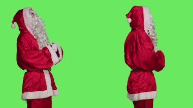 Noel Baba karakteri gibi davranan adam Noel arifesi ve tatil sezonunda pozitifliğini yayıyor. Geleneksel kış kostümü giyen şenlikli model yeşil ekran arka planında poz veriyor.