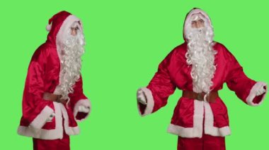 Kırmızı takım elbiseli neşeli insan Noel Baba gibi davranıyor, Noel ruhunu yeşil ekrana yayıyor. Geleneksel kostüm, şapka ve sakallı neşeli bir karakteri canlandıran mutlu bir adam..