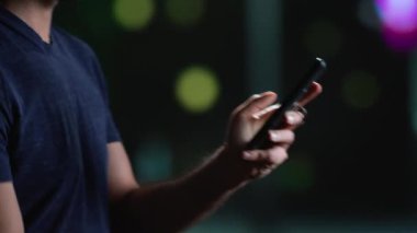 Gece geç saatlerde akıllı telefondaki modern insan aydınlanmış gökdelenlerle şehir merkezine bakıyor. Sıradan bir adam telefonda mesajlaşıyor ve şehir merkezinde yürüyor. El kamerasıyla. Kapat..