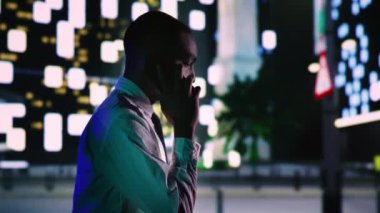 İş adamı gece şehir gezintisinde telefonla görüşüyor, kaldırımda gezinti yapıyor. Akıllı telefondaki Afrikalı Amerikalı şehir merkezindeki iş yerinin yakınlarında akşam yürüyüşünün tadını çıkarıyor. El kamerasıyla..