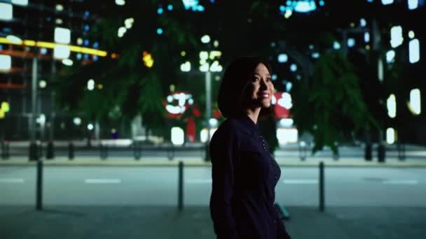 市内中心部の近くを歩くアジア人女性は オフィスビルや街灯で都市景観を賞賛しています 夜に街を散策するカジュアルな人 ダウンタウン地区の遊歩道 — ストック動画