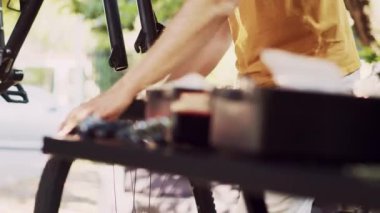 Genç ve aktif bir adam hassas bir şekilde tekerleği ayırıyor ve ön çatalı ve kulaklığı güvenli bir şekilde dışarıda bisiklet sürmek için ayarlıyor. Kırık modern bisikleti tamir eden ve ayarlayan erkek bisikletçilere yakın çekim.