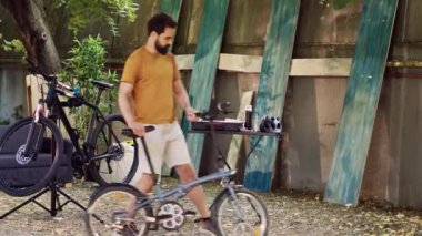 Spor düşkünü erkek bisikletçi, geleneksel yaz bakımı olarak ev bahçesinde bisiklete biniyor. Sağlıklı beyaz adam bisiklet tekerleklerini kontrol ediyor ve güvenli bisiklet sürmek için açık havada incelikle ayarlıyor..