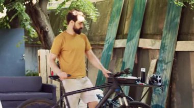 Açık hava beyaz adam bisiklet bakımı için özel aletler hazırlıyor. Genç erkek bisikletçi, ev bahçesinde modern bisikleti tamir etmek için alet çantasını kontrol ediyor..