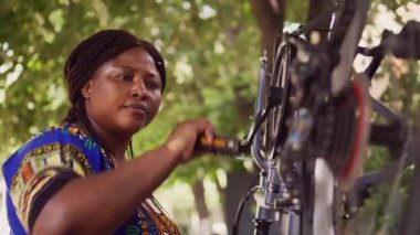 Kendini spora adamış Afrikalı Amerikalı kadın pedalları çevirerek bisiklet parçalarının performansını kontrol ediyor. Aktif kadın bisikletçi. Evin bahçesinde bisiklet tekerleğinin yakın plan lastiğinin düzgün çalışmasını sağlıyor..
