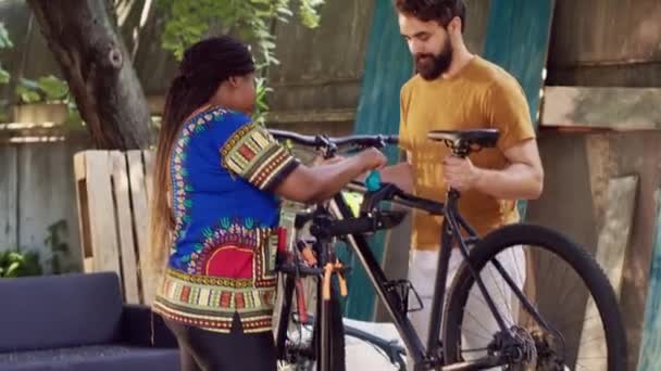 アフリカ系アメリカ人女性と自宅の庭で修理するための修理スタンドで自転車を調整する運動選手 スポーティな慎重なボーイフレンドは 外で自転車を再設計するガールフレンドからの助けを受け取ります — ストック動画