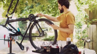 Çevrimiçi talimatları takip ederek dışarıda tabletini kavrayan enerjik beyaz erkek bisiklet tekerleğini ustalıkla ve titizlikle tamir ediyor. Akıllı aygıtla bisiklet parçalarını koruyan sportif adam.