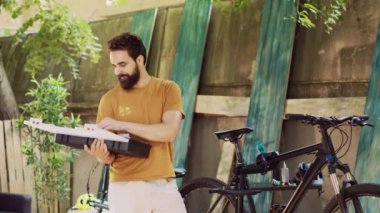 Atletik beyaz adam, yazın bisiklet bakımına hazırlanmak için çeşitli özel çalışma araçlarını inceliyor ve düzenliyor. Bahçede spor düşkünü bir erkeğin bisiklet alet çantasını taşıması ve kontrol etmesi.