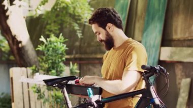 Spor meraklısı bir adamın alet çantasını taşırken ve kontrol ederken çekilmiş portre fotoğrafı bahçede yıllık bisiklet bakımına hazır. Kırık bisikleti tamir etmek için özel alet çantası kullanan hevesli bir erkek bisikletçi..