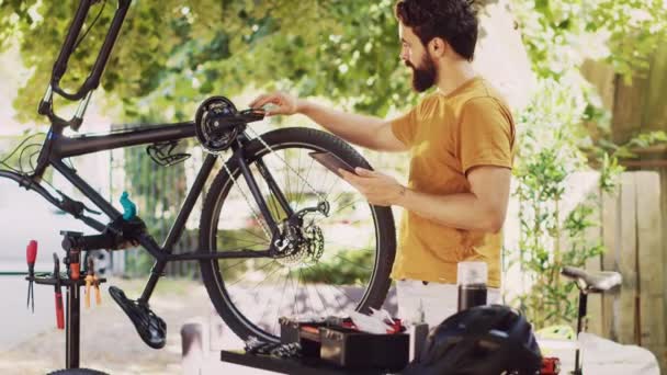 精力充沛的高加索男性按照在线指令从外面抓起他的平板电脑 熟练而精确地修理自行车轮毂 机灵的男子用智能装置保养自行车零件 — 图库视频影像