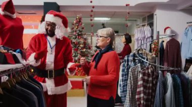 Alışveriş merkezinin etrafında Noel Baba kostümü giymiş yaşlı bir kadınla sohbet ediyor. Kıdemli müvekkil kırmızı giysisini gösteren tatil temalı takım elbiseli bir denetçi