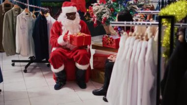 Noel Baba gibi davranan Afrikalı Amerikalı menajer Noel ağacının yanında bayram süsleri satan bir mağazada kadınla oturuyor. Moda butik yöneticisi müteşekkir müşteriye hediye sunuyor.