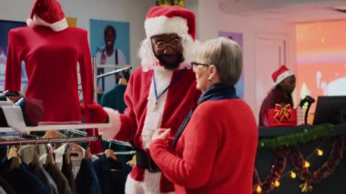 Noel Baba kostümü giyen ve gözlük takan çalışanlar, alışveriş merkezindeki yaşlı müşterilere Noel partisi kıyafetleri için gereken kırmızı bluzu bulmalarında yardım ediyorlar. İşçi, Noel tatilinde moda dükkanında yaşlı kadınlara yardım ediyor.