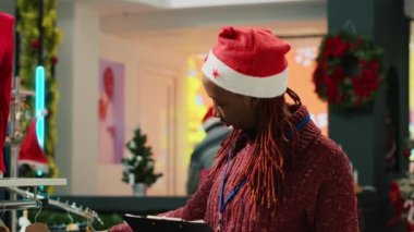 Mağaza müdürü Noel Baba şapkası takıyor alışveriş merkezinde pano tutuyor elbise raflarını denetliyor ve müşterileri selamlıyor. Xmas 'da çalışan bir yönetici moda butiğini süslüyor.