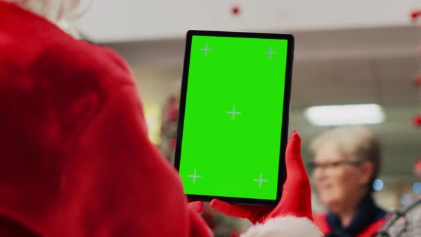 圣诞节装饰过的购物中心男演员假扮圣诞老人拿着彩色按键平板电脑 休息一下 在模拟屏幕上观看视频 而顾客则四处游荡 — 图库视频影像
