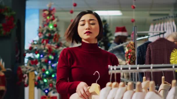 在寒假期间 一个快乐的女人在圣诞装饰服装店的架子上浏览华丽的外套 这就是她的肖像 微笑客户检查时尚精品 — 图库视频影像