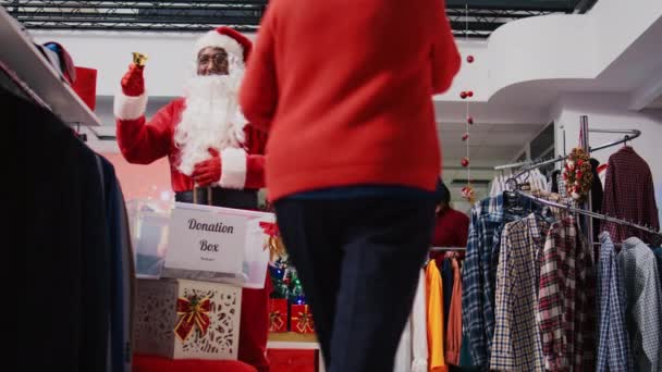 在服装店里穿着圣诞老人服装的工作人员助理从捐赠容器里的利他主义客户那里收集衣服 在圣诞节慈善活动中作为礼物送给他们 — 图库视频影像