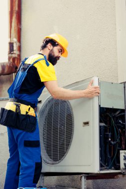 Sertifikalı teknisyen bozuk klimayı tamir etmek için sözleşmeli. Bozuk iç parçaları kontrol etmek için kondansatör ön bobin paneli sökülüyor. Elektrikçi uygun olmayan kabloları kontrol etmek için hvac sistemi açıyor