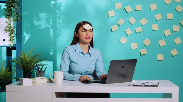 Playful asian employee having fun in colourful bright office, playing charades with coworker during online video call. Happy cheerful secretary in modern relaxed workplace over blue studio background