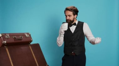 Otel hademesi kamerada kahve fincanının keyfini çıkarıyor. Komi, profesyonel üniforma ve eldiven giyiyor. Şık bir kapıcı serinletici içiyor, mavi arka planda bavulla poz veriyor..