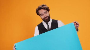Zarif uşağın elinde sarı arka planda boş mavi pankart var. Büyük reklam panolarında kopyasal alan var. Profesyonel çalışan kamerada boş kartonla poz veriyor, iyi yemek endüstrisi..