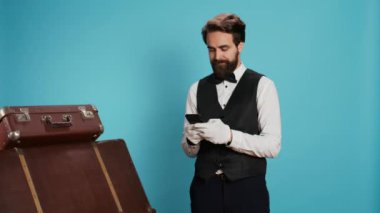 Kapıcı internetteki rezervasyonları gözden geçirmek ya da mesajlaşmak için akıllı telefon kullanarak sosyal medya uygulamasını kamerada tarıyor. Profesyonel otel hademesi cep telefonuyla mesaj atıyor, stüdyo fotoğrafı..