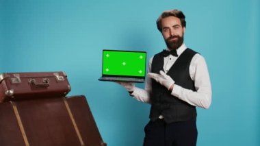 Kaliteli belboy stüdyoda dizüstü bilgisayarda sunar. Bavul yığınının yanında eldiven giyer. Lüks bir otelde çalışan deneyimli bir kapıcı, izole edilmiş bir model gösteriyor..