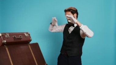İyimser kapıcı dans ediyor ve modern şarkılarla eğleniyor. Mavi arka planda duruyor. Çalışan kulaklıkla ses melodilerini seviyor, dans figürlerini gösteriyor..