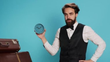 Kapıcı, kamerada duvar saatini gösteriyor, saati kontrol ediyor ve otel seyahat sektöründe dakik olmaya çalışıyor. Stüdyoda alışveriş çantalarının yanında saat ve dakikaları görmek için otel kapıcısı kullanan bir adam..