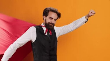 Lüks restoranda, sarı stüdyoda süper insan gibi davranırken kamerada kırmızı pelerinli zarif uşak pozu veriyor. Yiyecek ve içecek servisi yapan, kahraman kıyafeti giyen genç bir adam..