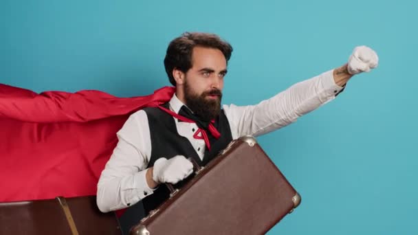 酒店行李员扮演超人与斗篷 主动提出帮助人们与手提箱行李在工作室 年轻的门卫以红色的面料表现出喜剧英雄的性格 下定决心 — 图库视频影像