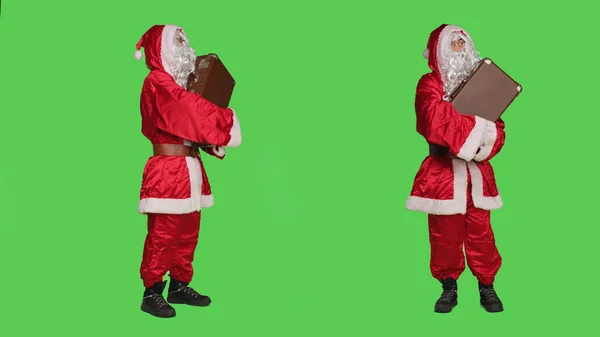 圣诞老人的服装与行李箱 等待运输通过全身绿屏背景 年轻人就像圣诞老人一样提着老式公文包 带着度假的念头 — 图库照片