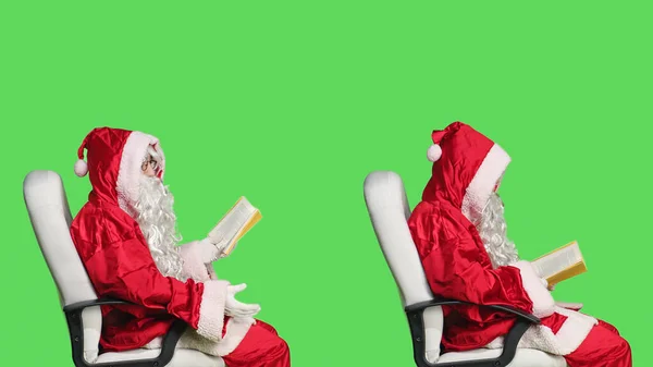 圣尼克在镜头前阅读诗集 欣赏文学或小说教育讲座 穿着像桑塔的男人坐在椅子上 手里拿着新奇的故事 背景是绿屏的 — 图库照片