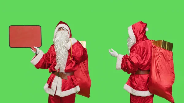 サンタキャラクターは マーケティング目的 季節の冬のお祝いのために赤いスピーチバブルを使用して広告を作成します スタジオでグリーンスクリーン上の空の掲示板を示す父クリスマス — ストック写真