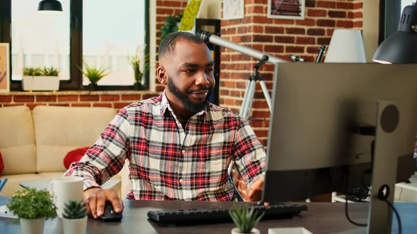 疲れた眠いアフリカ系アメリカ人従業員がリモートで作業し コンピュータにデータを入力し すぐに仕事を終えることに満足しています 暖かい居心地の良いリビングルームのアパートでの仕事の電子メールに答えるテレワーカー — ストック写真