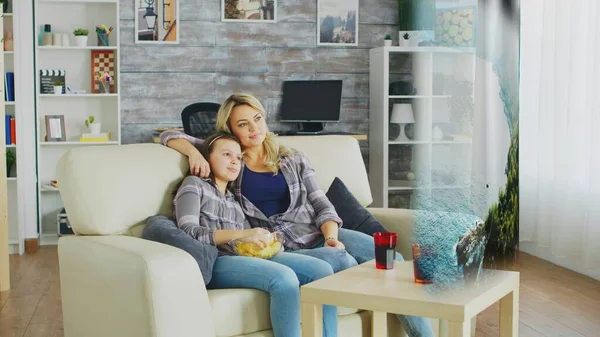 Happy family looking at nature documentary on AR projector display. Mother and daughter relaxing at home on couch, hugging and watching internet content on streaming services