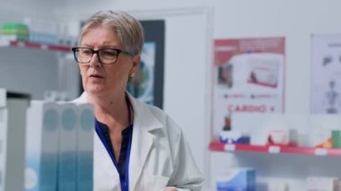 Eczacı dükkanındaki yaşlı eczacı elinde alışveriş sepeti, raflardaki ürünleri düzenliyor. Eczanede ilaç paketleri düzenleyen usta bir eczacı.