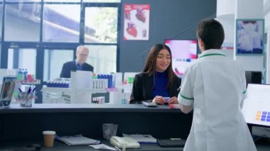 Eczanedeki Asyalı kadın eczane ürünleri almak için kredi kartı kullanıyor. Gülümseyen bir müşteri, ihtiyacı olan ilaçları aldıktan sonra eczanede ücretsiz ödeme yapıyor.