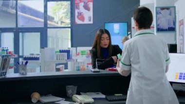 Eczanedeki müşteri eczane kasasında tıbbi malzeme almak için kredi kartı kullanıyor, eczacı da poşetleme işlemi için yardım ediyor. Müşteri eczanede ücretsiz ödeme yapıyor.
